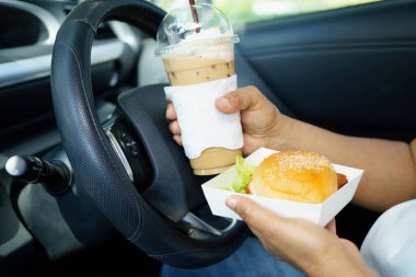 Asyalı kadın sürücü arabada hamburger yiyerek bekliyor..