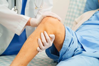 Doktor, hastanede dizinde yara izi olan Asyalı yaşlı kadın hastayı kontrol ediyor..