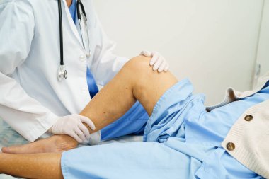 Doktor, hastanede dizinde yara izi olan Asyalı yaşlı kadın hastayı kontrol ediyor..