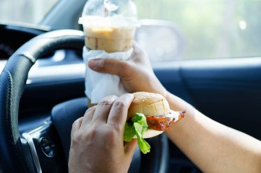 Asyalı kadın sürücü arabada hamburger yiyerek bekliyor..