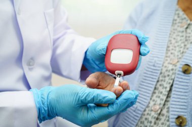 Diyabet tedavisinde kan şekeri seviyesini kontrol etmek için dijital glikoz ölçer kullanan Asyalı doktor.