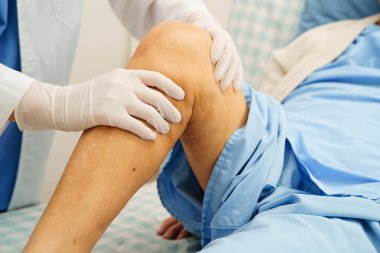 Doktor, hastanede dizinde yara izi olan Asyalı yaşlı kadın hastayı kontrol ediyor..