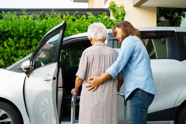 Bakıcı, Asyalı yaşlı kadın engelli hastaya arabaya binmek için yürüteç kullanmasında yardım ediyor..