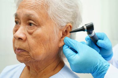 Otolaryngologist ya da ENT hekim doktoru yaşlı hasta kulağını otoskopla muayene ediyor, işitme sorunu var..