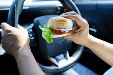 Asyalı kadın sürücü arabada hamburger yiyerek bekliyor..