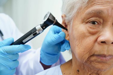 Otolaryngologist ya da ENT hekim doktoru yaşlı hasta kulağını otoskopla muayene ediyor, işitme sorunu var..