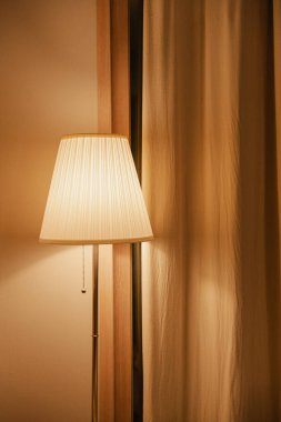 Bej perdelerin yanında zarif bir lamba.