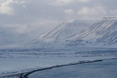 Karlı dağ zirveleri bulutlu gökyüzünün altında güneş ışığı ile