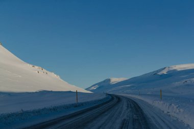 Karlı yol mavi gökyüzünün altında, açık kırsalda dönüyor.