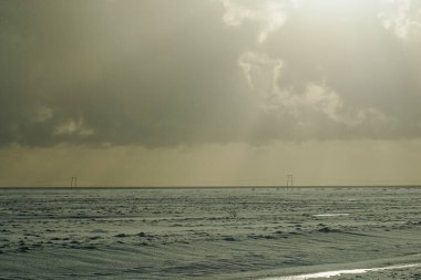 Geniş karlı alan, uzak elektrik hatları ve bulutlu gökyüzü.