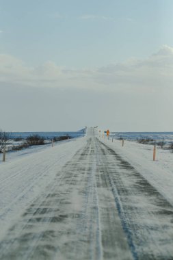 Açık gökyüzünün altında ufka uzanan uzun karlı bir yol.