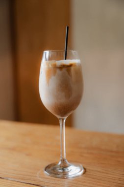 Sütlü buzlu kahvenin yakın planında, ahşap bir masada uzun bir bardakta.