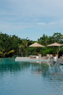 Şemsiyeli ve şezlonglu sakin havuz kenarı sahnesi.