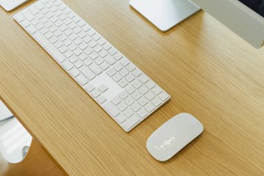 Beyaz klavyesi ve faresi olan temiz ahşap masa, üretkenlik veya yaratıcılığa hazır modern bir çalışma alanı öneriyor..