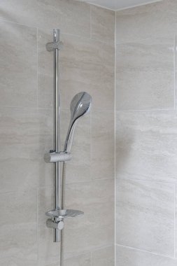 Kapalı çekimde ışığa karşı krom duş armatürü, nötr fayanslı duvar, minimalist banyo tasarımı.. 