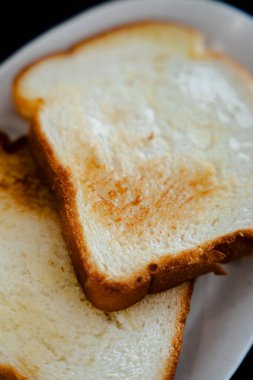 Tabağa istiflenmiş iki dilim altın sarısı tost. Tost tereyağlı ve yemeye hazır..