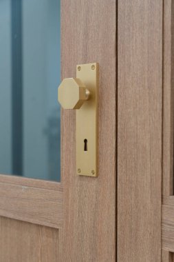 Açık renkli ahşap bir kapıya dayanan, şık, sekizgen bir altın kapı tokmağının olduğu iç kapının yakın çekimi..
