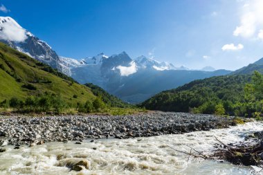 Gürcistan 'ın Svaneti bölgesinde Mestia köyü yakınlarındaki macera yürüyüş rotasında dağlarla ve nehirle birlikte yürüyüş yapmak..