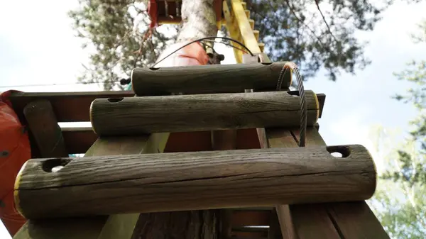 Macera Parkı 'ndaki Merdiven Basamakları' nın yakınından Ağaç Platformu 'na giden bir yakın plan macera parkındaki merdivenlere odaklanarak ziyaretçilere ağaç platformuna kadar rehberlik ediyor. Metal ip ve yukarıya doğru çıkan başka bir merdiven görünüyor.
