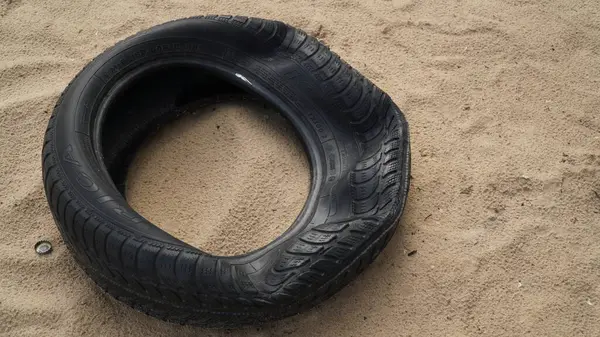 Kum Lastiği Patlak: Hasarlı Lastik Bir Tarafta Patlak Görüntü, kumda duran hasarlı bir lastiği tasvir ediyor. Lastiğin bir tarafı patlamış, bu da hasar ya da delinme olduğunu gösterir. Kumun üzerindeki pozisyonu, hasarın Dr.
