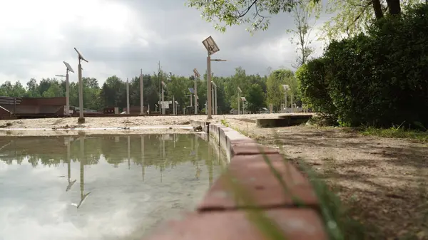 Güneş enerjisiyle çalışan sokak lambaları olan Lake and Beach bir gölü kumlu plajdan ayıran duvarın perspektifinden çekilmiş manzaralı bir fotoğraf. Arka planda, güneş enerjisiyle çalışan sokak lambaları görülebiliyor ve modern, sürdürülebilir bir altyapı dokunuşu eklenebiliyor.