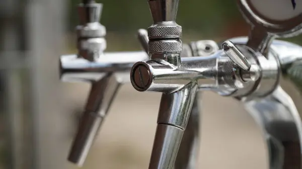 Silver Beer Taps 'in yakın plan çekimi. Parlak gümüş bira musluklarının yakın plan çekimi. Detayları ve ekipmanların işçiliğini vurguluyor. Cilalı metal parıldıyor, temizliği ve bir bar veya bar ortamında kullanılmaya hazır olmayı gösteriyor. Bu...