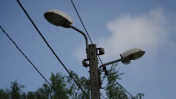 Arka planda Huş Ağacı ve Yüksek Voltajlı Elektrik Hatları ile Eski Elektrik Kutbu 'ndaki İki Sokak Işığının Yakın Çekimi Arka planda bir huş ağacı ve yüksek voltajlı elektrik hatlarıyla eski bir elektrik direğine monte edilmiş iki sokak lambasının yakın görüntüsü.