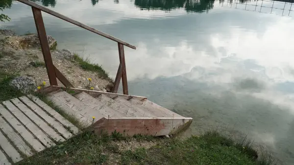 Arka planda Kayalıklar ve Leontodon hispidus 'la göle giden tahta merdivenler var. Arka planda ise kayalar ve Leontodon hispidus bitkisi var. Ahşap merdivenler trana erişim sağlar.