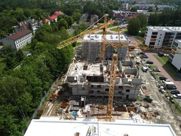 Vinçlerle birlikte kentsel inşaat alanının hava görüntüsü dört katlı bir apartmanın kentsel şantiyesini yakalıyor. İnşaat kaosunun ortasında iki sarı turna aktif olarak çalışıyor. Site yeşilliklerle çevrili.,