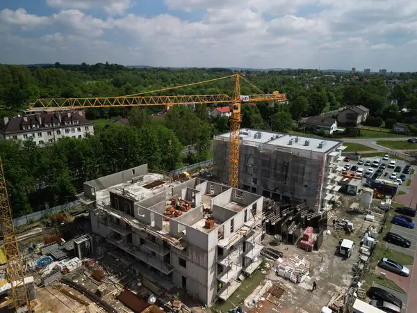 Crane 'in İkametgâh İnşaat' ta çalışırken drone görüntüsü İHA 'nın çektiği bir vinç, konut inşaatında çalışırken tek bir vinci çekiyor. Arka planda, yeşillik birkaç yüksek binası olan küçük bir şehir manzarasını çevrelemektedir.