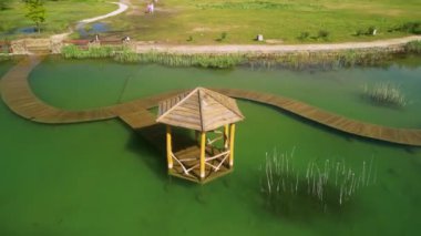 Serene Gazebo, Vibrant Green Lake Rıhtımı Havadan canlı yeşil bir göle giden ahşap bir iskelenin manzarası Serene Gazebo, Vibrant Green Lake Havalimanı, ahşap bir rıhtım manzarası..