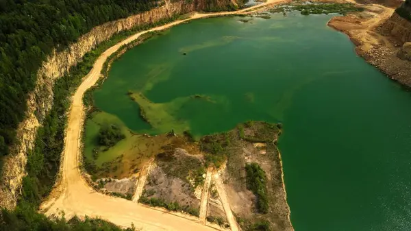 Quarry Gölü 'nün çevresindeki uçurum ve ormanı çevreleyen havadan görüntüsü sol ve yoğun ormandaki sarp dolomit kayalıklarıyla çevrili büyük bir taş ocağı gölü ve çarpan yeşil su görüntüsünü yakalar. Kum yolları suyun kenarından geçer, yol gösterir.