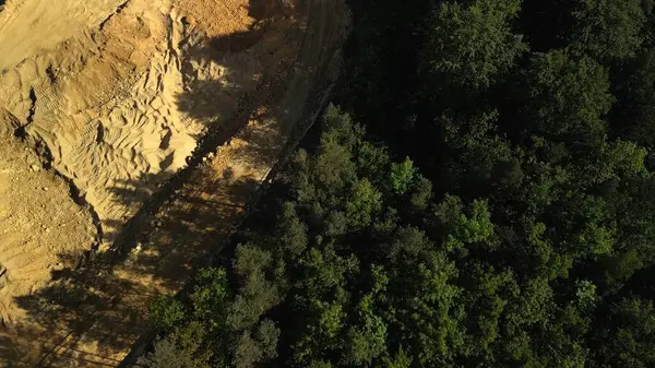 Kum ocağının havadan görünüşü. Kum ocağının en üst manzarası. Bu hava görüntüsü, sarı bir açık çukur dolomit ocağı ile yemyeşil alanlar arasında çarpıcı bir tezat gösteriyor. Görüntü görsel olarak bölünmüş, taş ocağı sol tarafta ve canlı bir açgözlülükle dolu.
