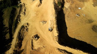 Kamyon ve Toz Bulutları ile Açık-Pit Quarry 'nin hava görüntüsü İHA' dan bu hava görüntüsü açık bir maden ocağına tepeden aşağı bir perspektif sunuyor, toz bulutlarıyla çevrili hareket halindeki bir kamyonu içeriyor. Görüntü Mi 'nin dinamik aktivitesini yakalar.