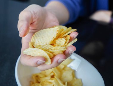 Kadın elini bir kaseden patates cipsi almak için kullanıyor..