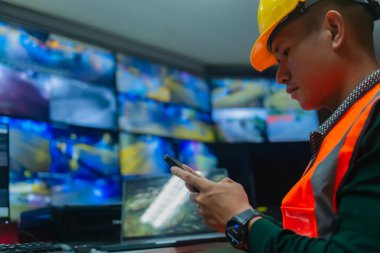 Bir adam birkaç monitörün önünde oturuyor, telefonuna bakıyor ve trafik raporunu yazıyor.