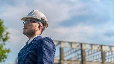 Asyalı yetişkin ustabaşı inşaat projesinin önünde duruyor ve bir inşaat projesini kararlılıkla inceliyor. Mühendis inşaatı denetliyor..