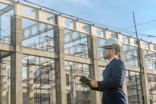 Asyalı yetişkin ustabaşı inşaat projesinin önünde duruyor ve bir inşaat projesini kararlılıkla inceliyor. Mühendis inşaatı denetliyor..