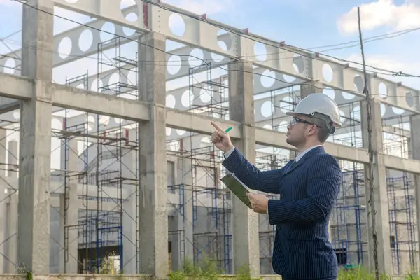 Asyalı yetişkin ustabaşı inşaat projesinin önünde duruyor ve bir inşaat projesini kararlılıkla inceliyor. Mühendis inşaatı denetliyor..