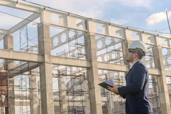 Asyalı yetişkin ustabaşı inşaat projesinin önünde duruyor ve bir inşaat projesini kararlılıkla inceliyor. Mühendis inşaatı denetliyor..