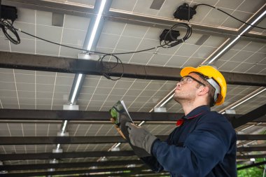 Mühendis teknik servisi, kurulum güneş pili panelini kontrol ediyor ve panodaki tüm listeleri ve güneş paneline düzgün bağlanan kabloları kontrol ediyor.