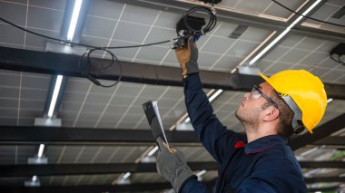 Mühendis teknik servisi, kurulum güneş pili panelini kontrol ediyor ve panodaki tüm listeleri ve güneş paneline düzgün bağlanan kabloları kontrol ediyor.