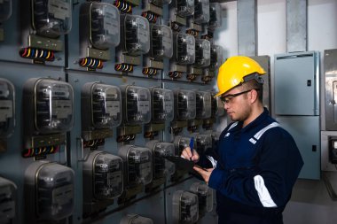 Elektrik bakım mühendisi kontrol ediyor. Elektrik sayacı, ana dağıtım panosu ve bir panoya elektriğin değerini yazın.