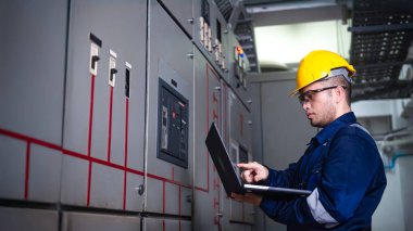 Elektrik mühendisi ana elektrik kontrol panelleri ve anahtarlar, dizüstü bilgisayardaki kayıt değerleri, elektrikçi fabrikadaki elektrik sistemlerini kontrol ediyor..