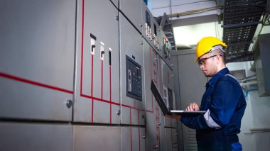 Elektrik mühendisi ana elektrik kontrol panelleri ve anahtarlar, dizüstü bilgisayardaki kayıt değerleri, elektrikçi fabrikadaki elektrik sistemlerini kontrol ediyor..