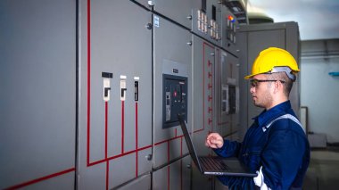 Elektrik mühendisi ana elektrik kontrol panelleri ve anahtarlar, dizüstü bilgisayardaki kayıt değerleri, elektrikçi fabrikadaki elektrik sistemlerini kontrol ediyor..