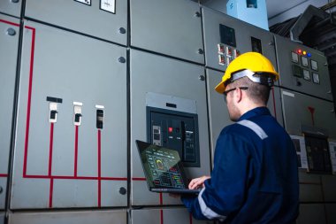 Elektrik mühendisi ana elektrik kontrol panelleri ve anahtarlar, dizüstü bilgisayardaki kayıt değerleri, elektrikçi fabrikadaki elektrik sistemlerini kontrol ediyor..