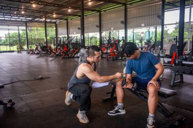 Bir özel antrenör, stajyere spor salonunda nasıl egzersiz yapılacağını öğretiyor.