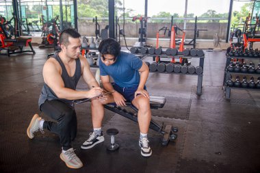 Erkek antrenör, bir fitness merkezinde fiziksel formlarını geliştirmek isteyen bir müşteri için egzersiz programı hazırlıyor.