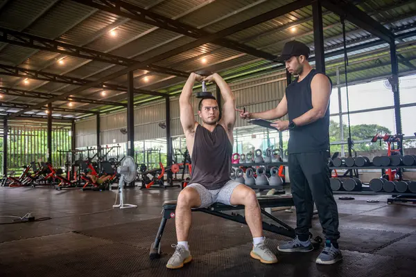 Bir özel antrenör, stajyere spor salonunda nasıl egzersiz yapılacağını öğretiyor.